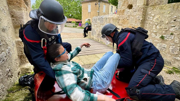 Deux pompiers casqués mettent une victime fictive sur un brancard rouge dans une ruelle