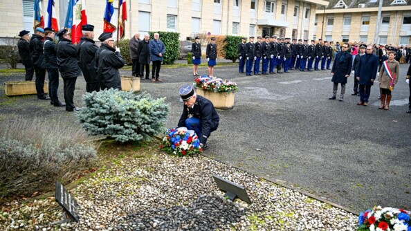 Un gendarme dépose une gerbe de fleurs. Derrière lui, des autorités civiles et militaires. Sur le côté, six porte-drapeaux, et en arrière-plan, les troupes au garde-à-vous.