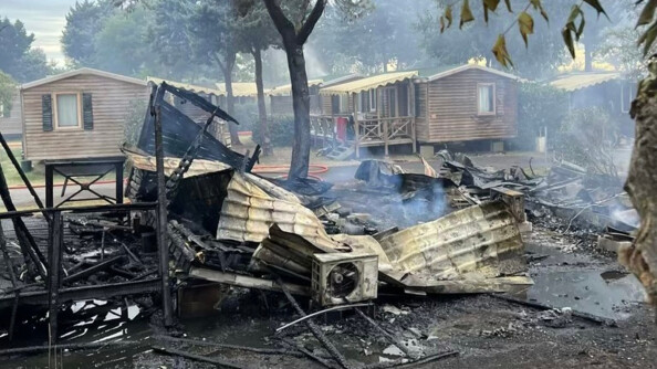Photo montrant un mobil-home intégralement brûlé au premier plan et trois bungalows intacts en arrière-plan.
