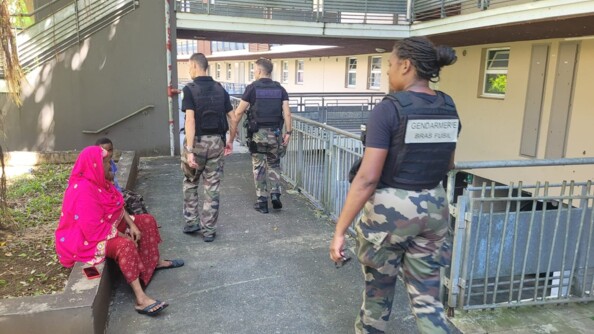 Des gendarmes marchent dans une all&eacute;e, longeant un immeuble, passant &agrave; c&ocirc;t&eacute; d'habitants assis sur un muret, apr&egrave;s le passage du cyclone Garance sur l'&icirc;le de la R&eacute;union.