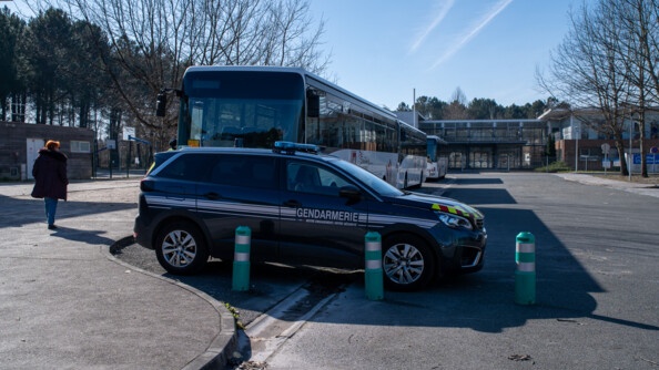 Une voiture de gendarmerie devant des bus, le tout devant un établissement scolaire.