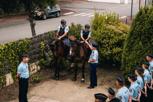 Le directeur général de la gendarmerie se tient debout aux côtés de deux gendarmes assis sur leur cheval. Il serre la main de l'un des deux militaires