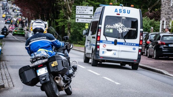 Un motocycliste d'EDSR vu de dos, assurant l'escorte de la fin de course où se trouve un véhicule de secours.