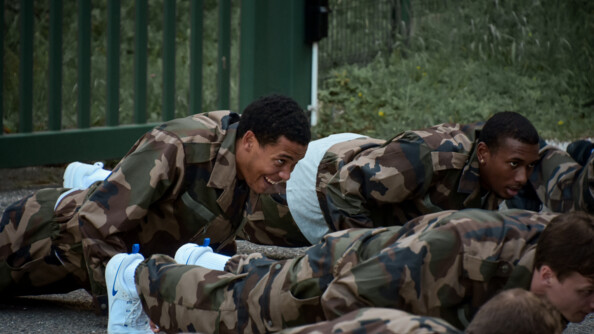 Quatre hommes en treillis kaki de trois-quarts face, en train de faire des pompes.