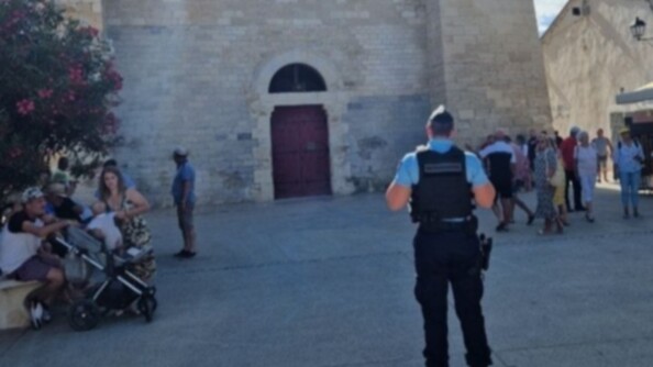 En extérieur, un gendarme surveillent la place devant l'église où de nombreux croyants se préparent à entrer.