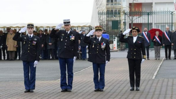 Quatre personnes, autorités civiles et militaires, au garde-à-vous. Dans le fond, un parterre d'invités, dont trois sur la droite arborent une écharpe tricolore.