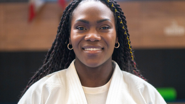 Clarisse Agbégnénou, judokate française, pose en kimono blanc, souriante, face à l'objectif. Elle porte des anneaux dorés aux oreilles et des dreadlocks.