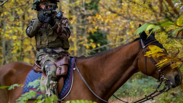 Un cavalier de la garde en treillis, casque sur la tête, sur sa monture, au milieu des bois, vise avec son Famas.