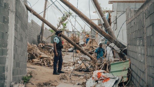 Un gendarme au milieu des ruines d'habitations. A c&ocirc;t&eacute; de lui se trouve quelques habitants.