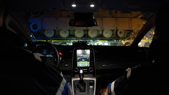 Deux gendarmes dans une voiture de la gendarmerie face aux chars américains. Il fait nuit et sombre.