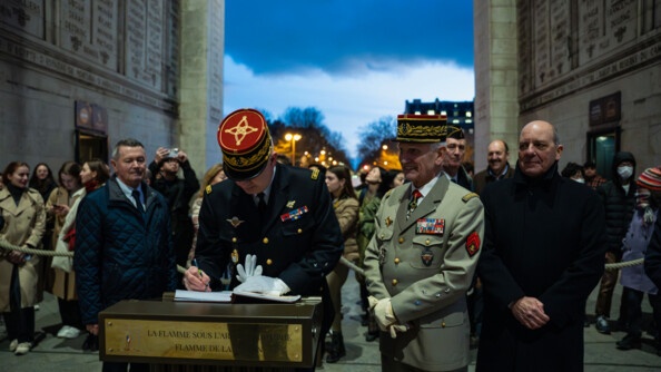 Un g&eacute;n&eacute;ral de gendarmerie en train de signer le livre de la flamme. A ses c&ocirc;t&eacute;s, un g&eacute;n&eacute;ral de l'arm&eacute;e de Terre et deux homme en civil.