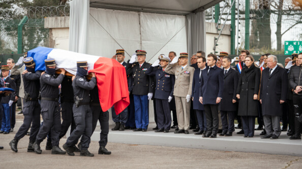 Au premier plan, le cerceuil du major Arnaud Blanc, recouvert du drapeau fran&ccedil;ais, port&eacute; par ses fr&egrave;res d'armes. Au second plan les autorit&eacute;s civiles et militaires : Emmanuel Macron, pr&eacute;sident de la R&eacute;publique, G&eacute;rald Darmanin, ministre de l&rsquo;Int&eacute;rieur et des Outre-mer, S&eacute;bastien Lecornu, ministre des Arm&eacute;es, le g&eacute;n&eacute;ral d&rsquo;arm&eacute;e Christian Rodriguez, directeur g&eacute;n&eacute;ral de la gendarmerie nationale, le g&eacute;n&eacute;ral d&rsquo;arm&eacute;e Pierre Schill, chef d'&eacute;tat-major de l'arm&eacute;e de Terre, le g&eacute;n&eacute;ral de division Ghislain R&eacute;ty, commandant le GIGN, ainsi que les pr&eacute;sidents du S&eacute;nat et de l&rsquo;Assembl&eacute;e nationale, G&eacute;rard Larcher et Ya&euml;l Braun-Pivet.