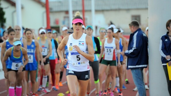Une femme en tenue de sport et portant une casquette rose s'élance pour courir. Derrière elle, plus floue, des dizaines de femmes sur une piste attendent de partir