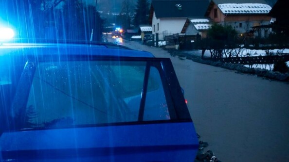 A la nuit tombante, un véhicule gendarmerie, vu de trois-quarts avant, portière avant ouverte et gyrophare allumé, stationné en bordure d'un chemin inondé au milieu des habitations.