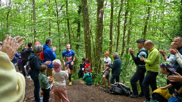 Un participant cours au milieu d'une foule qui l'encourage. La photo est prise en foret dans une montée, de jour.