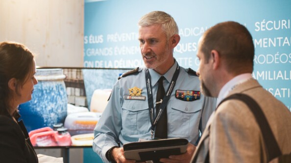 Un référent sûreté au centre de la photo, à droite une femme échange avec lui, à gauche un homme écoute, au stand du MIOM à l'ANCTour