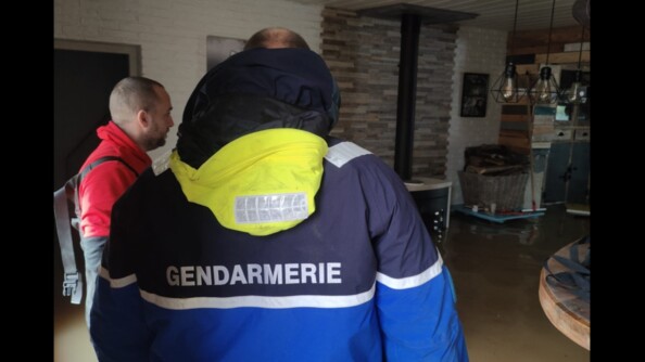 Un gendarme et un habitant dans une maison. L'eau, qui a inond&eacute; toute la maison, monte au niveau de leur taille.