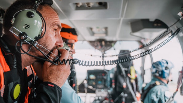 Vue dans un cockpit d'hélicoptère, un gendarme de profil tête nue, tient son micro près de sa bouche