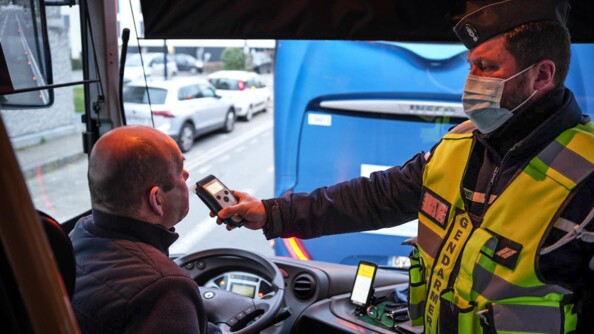 Un gendarme avec une chasuble jaune fluo, fait souffler un conducteur de bus assit derrière son volant.