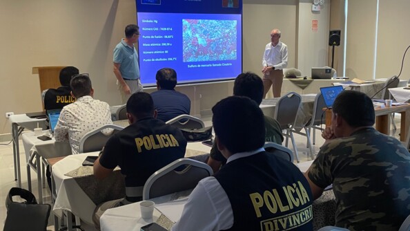 Au premier plan, des magistrats et des policiers péruviens vus de dos, assis dans une salle de classe. Face à eux, un officier de gendarmerie et un garde civil espagnol, en civil, à côté d'un grand écran où sont projetés des slides sur les atteintes environnementales (mercure).