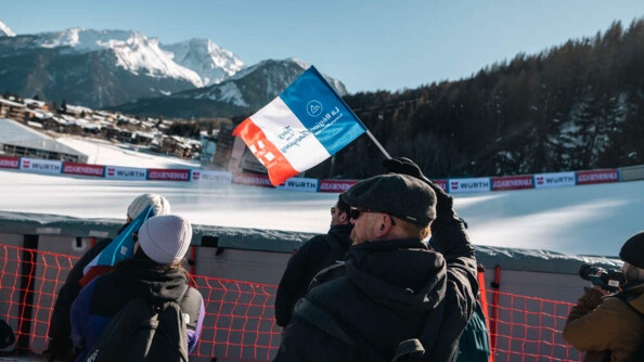 Des spectateurs de dos devant une piste de ski.