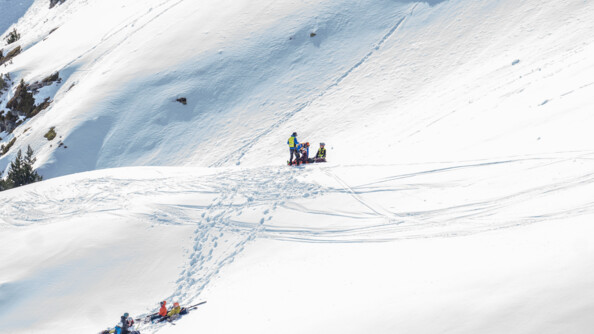 Dans la montagne enneigée, les gendarmes interviennent pour secourir un homme à terre. En contrebas, se trouve quatre personnes accompagnant l'individu pris en charge.
