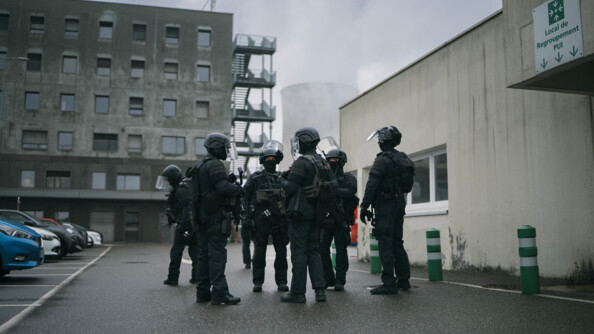 En extérieur devant la centrale, les gendarmes échangent avant le lancement de l'exercice. Ils sont en tenue d'intervention avec un casque et des protections.