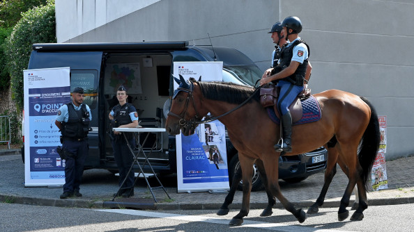 Deux gendarmes de la Garde républicaine patrouillent côte à côte, à cheval, à l'occasion du festival Garorock. derrière eux se trouve un véhicuyle de la gendarmerie, ainsi que deux gendarmes, debout devant un kakémono portant l'inscription "Point d'accueil"
