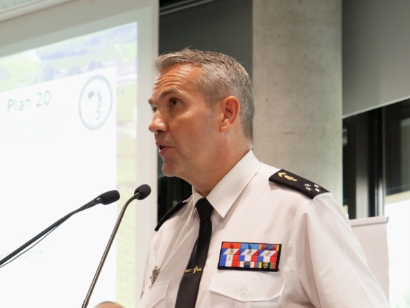 En buste de trois quart avant gauche, un gendarme en chemisette blanche cravate parle dans un micro